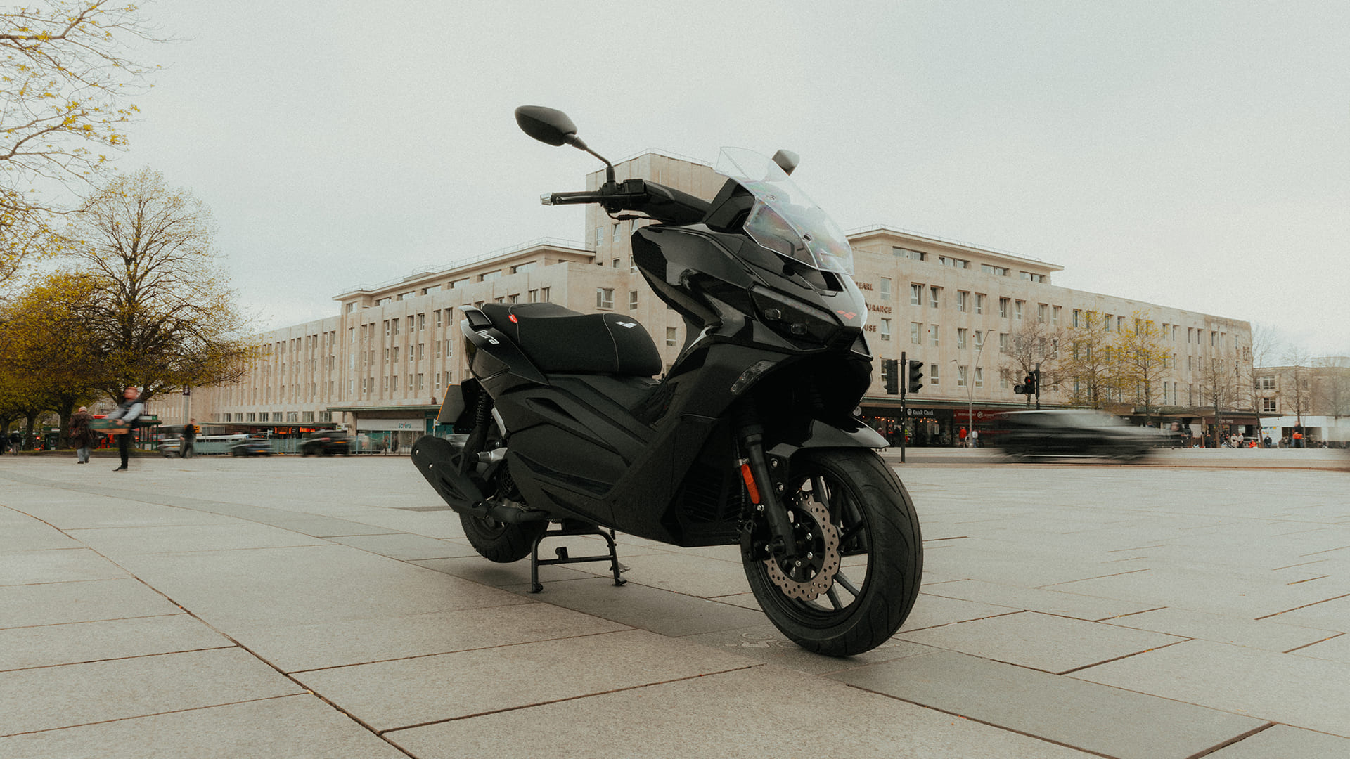 Aura 125 parked in city square with art deco building behind