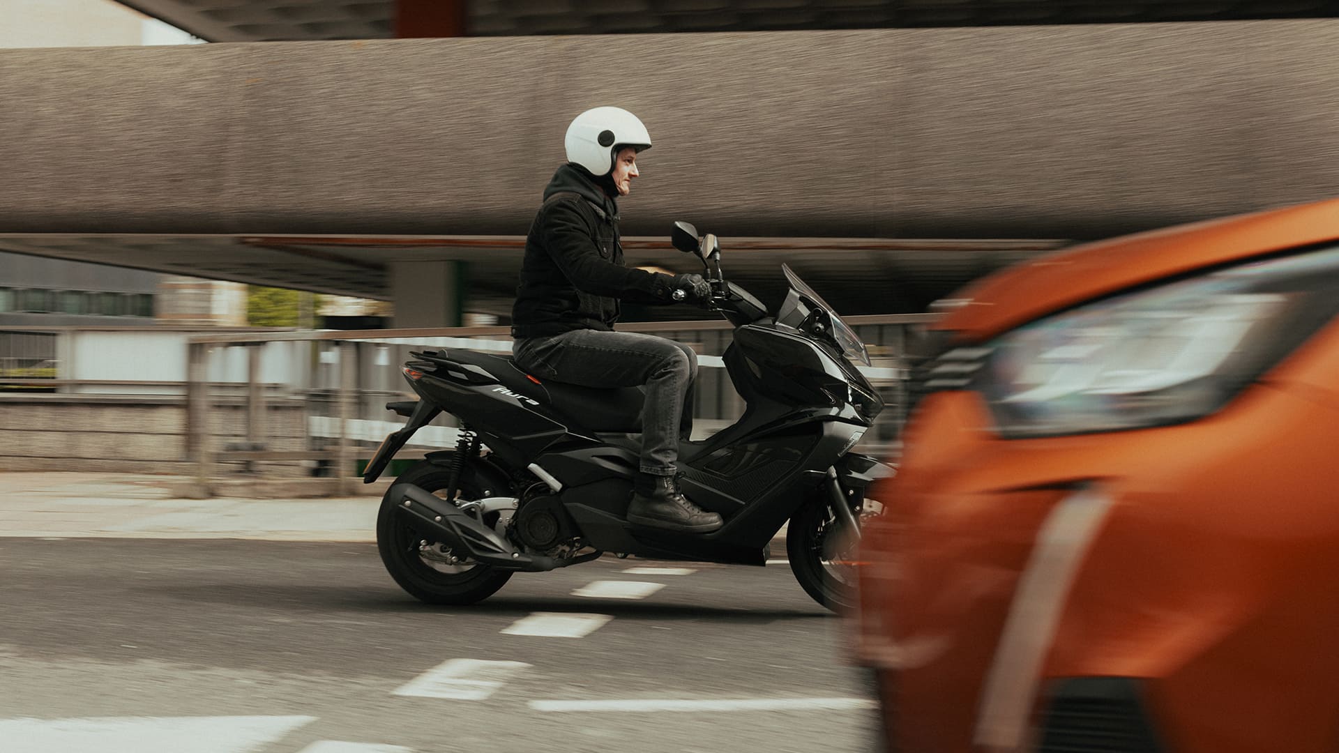 Rider on Aura 125 side view passing under concrete overpass